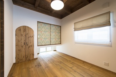 アーチ型の扉の中は将来お仏壇を置く予定。 普段の生活で広々使えるように床はリビングと同じボルドーパインのフローリングに。お客様が宿泊されるときは白と黒の市松柄の薄畳を敷いてモダン和風の部屋に模様替えします。