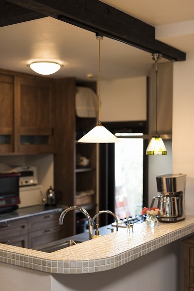 料理上手な奥さまに、収納物も細かく採寸して無駄のないオーダーキッチンを提案した。後のカップボードもリビングの雰囲気に合わせて無垢材で造作。目隠しカウンターの角を丸くしタイル張りすることで優しい印象に。お気に入りのレトロな照明も一つ一つ慎重にセレクト。
