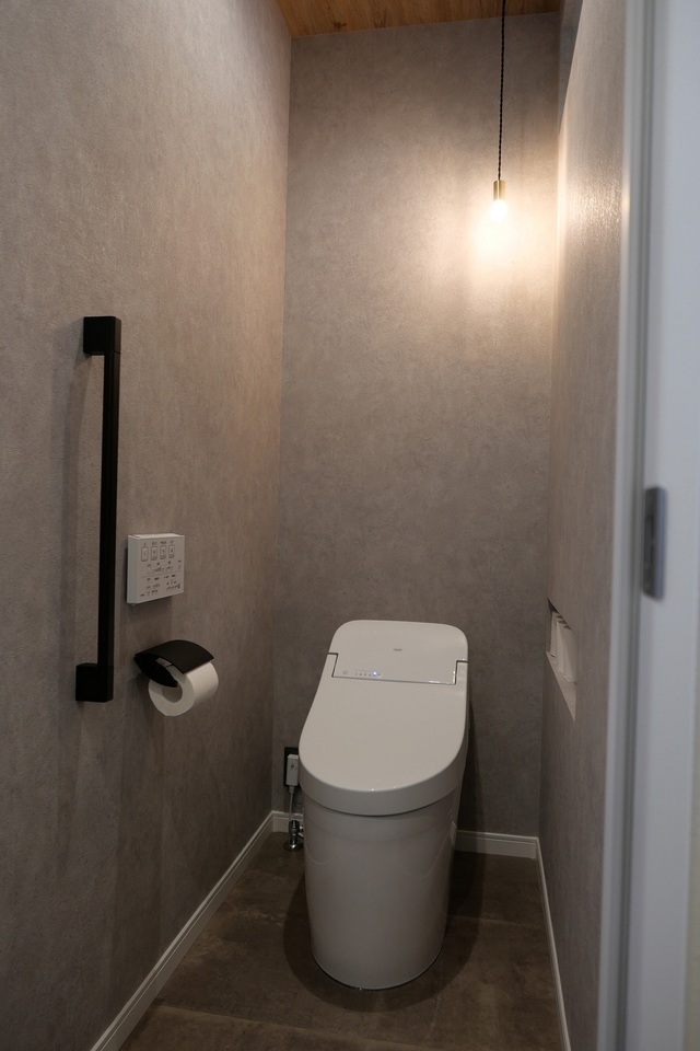 グレーの床と壁に合わせ、天井には木目をチョイス。優しい光のペンダントライト。外壁に面していないため、上部にFIXガラスを入れ脱衣所から自然光を取り入れるように工夫しています。
収納棚を設けずスッキリみせるため、トイレットペーパーを収納できるサイズのニッチを造りました。